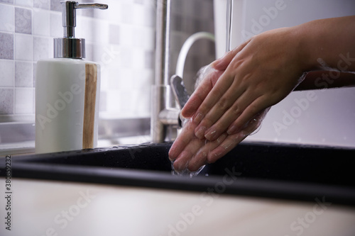 Cropped shot of an unrecognizable woman washing her hands in the kitchen sink at home
