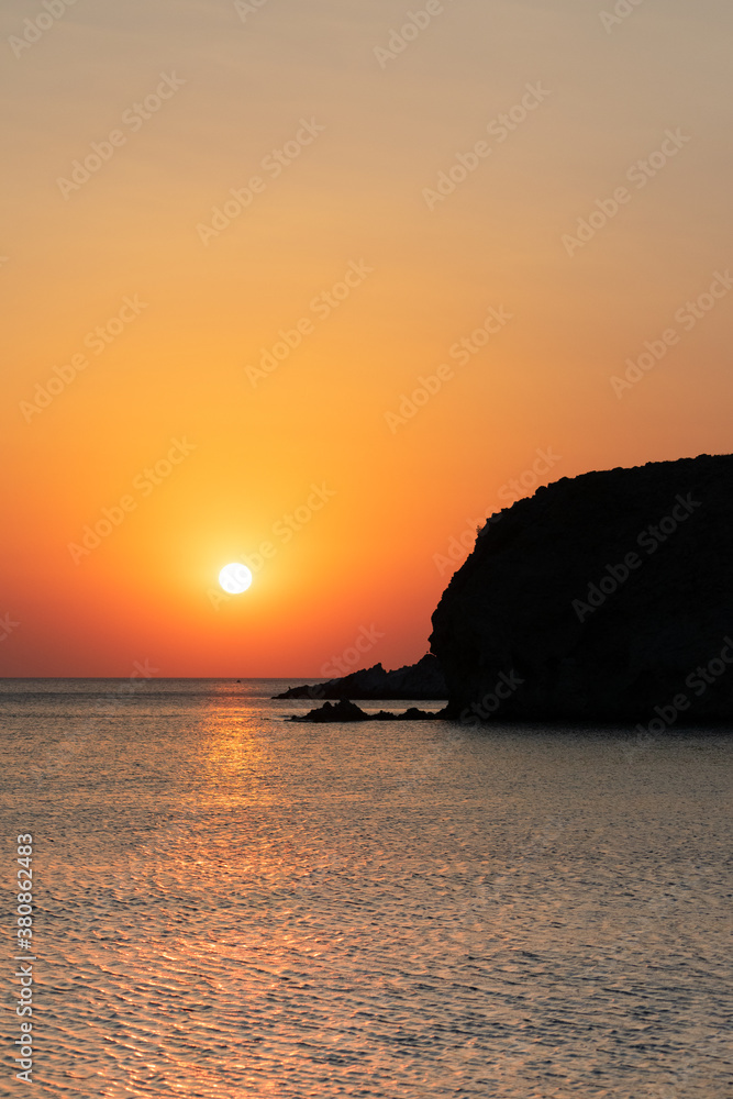 Sunset on the sea against the backdrop of the silhouette of a cape