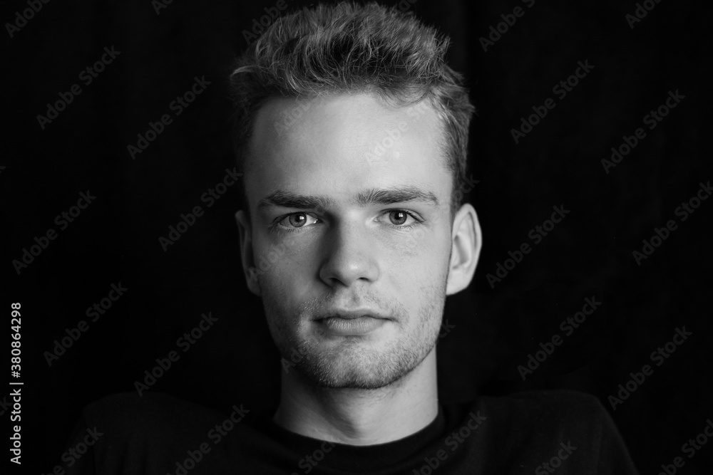 Portrait of a serious young guy on a dark background, black and white photo