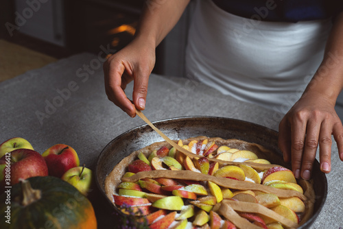 Preparation, Thanksgiving Day celebration. The chef decorates the surface of the pie with strips of dough, over the filling of colorful apples. Making a traditional apple pie.