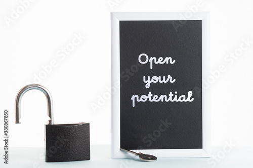 In a black-and-white frame, the inscription open your potential. Next to the frame is an open lock and key.