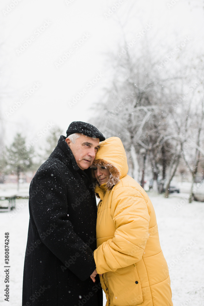 Old couple hugging outdoors in snowfall Old couple hugging outdoors in snowfall