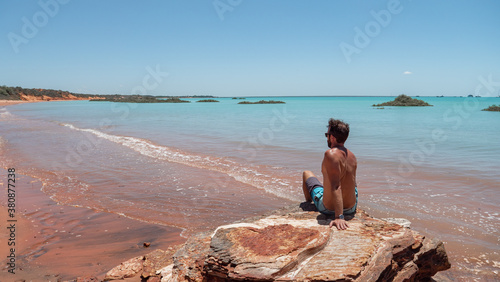 Man overlooking red sand beach and turquoise water