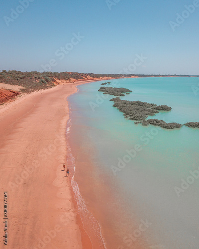 Couple walking on red sand beach and turquoise water photo