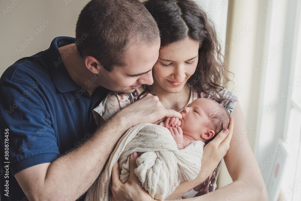Newborn baby in his parents' arms sucking on his father's little finger Newborn baby in his parents' arms sucking on his father's little finger