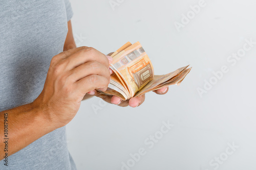 Young man in grey t-shirt counting euro banknotes , front view.