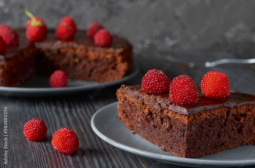 Piece of chocolate muffin with bright red berries close-up.In the background a dish with a whole muffin.