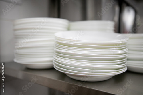 Stacks of many white plates on a wire rack shelf in a commercial kitchen