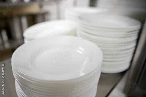 Stacks of many white plates on a wire rack shelf in a commercial kitchen