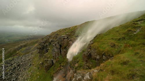 Waterfall high on Mallerstang Edge in Cumdria being blown upwards or inverted by the strong wind. As a shaft of sunlight highlights the waterfall a small rainbow appears in the upwards stream.