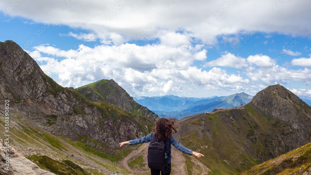 Young female tourist on the background of a mountain panorama. Standing with arms outstretched,