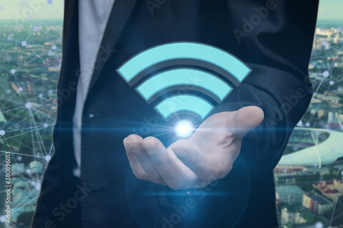 Fotografie A businessman holds a shining Wi-Fi icon against the city background
