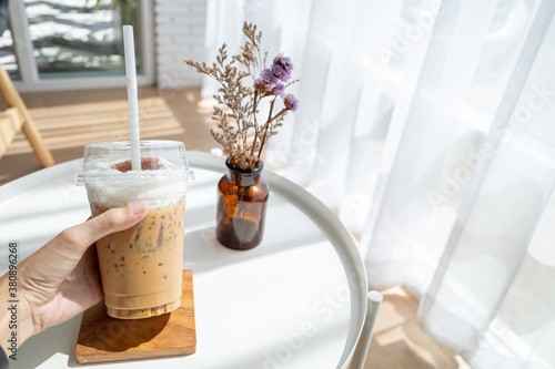 Woman holding plastic glass of iced coffee in coffee shop