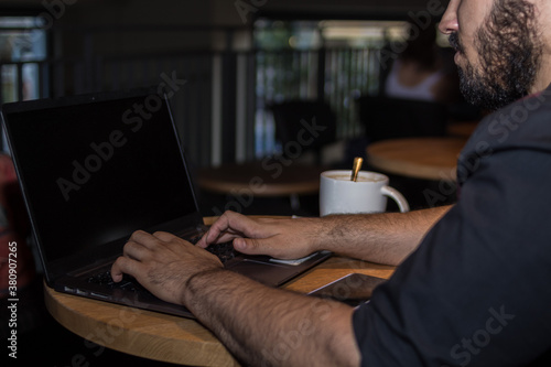 Young caucasian man with a black shirt in a shop working with his laptop having a coffee and with his phone