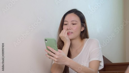 Onychophagia and onychophagy concept. Asian woman sitting on home stair has bite nails habit. asian woman sitting on home stair has bite nails habit. Female using mobile smart phone chewing nails.