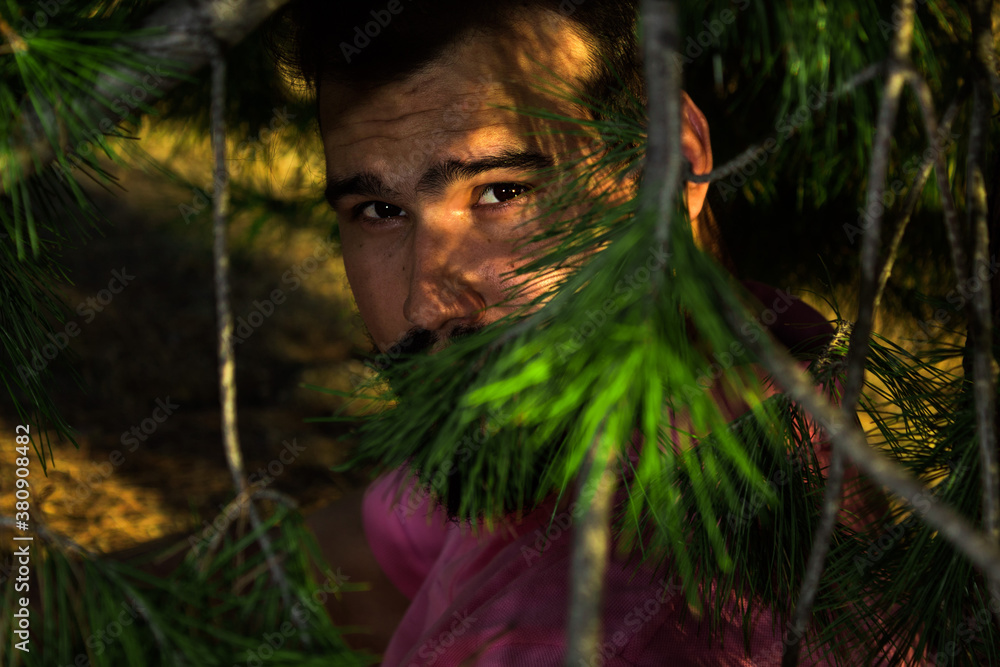 Portrait of caucasian man with beard and black hair in the forest through some branches Portrait of caucasian man with beard and black hair in the forest through some branches