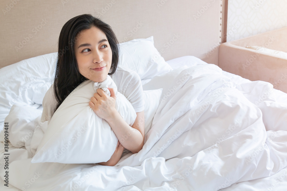 Attractive young beautiful girl stretching in the bed at home. Pretty young girl in white on bed in modern bedroom. Happy Cheerful Young woman on bed in modern bedroom after wake up.