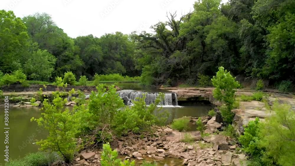 Zoom in video of a small waterfall flowing with stone and green trees. Zoom in video of a small waterfall flowing with stone and green trees.