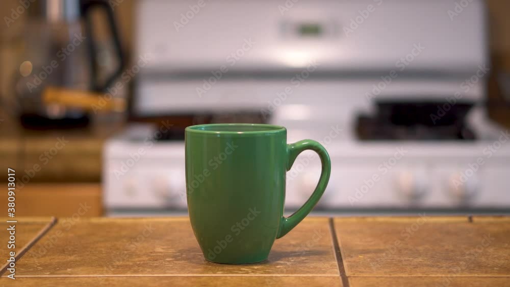 Steam rising off a green mug with kitchen background in soft focus Steam rising off a green mug with kitchen background in soft focus