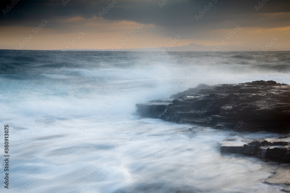 Rocky seashore with wavy ocean and waves crashing on the rocks.