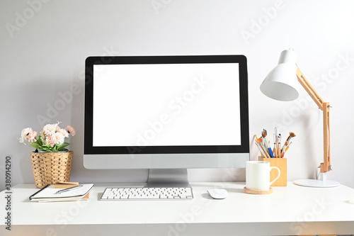 Mock up image of computer pc with white screen, coffee cup, plant, lamp and office supplies on minimal work desk.