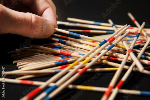 Mikado board game for the development of fine motor skills on a dark background. The man's hand just pulls one game stick from under the other