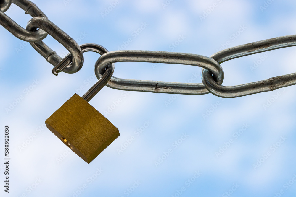 Chrome padlock and strained steel chains close up against blue clouded sky symbolizing lockdown Chrome padlock and strained steel chains close up against blue clouded sky symbolizing lockdown