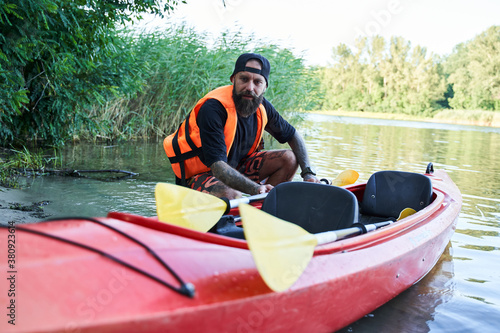 Close up shot man sitting near canoe on sandy beach