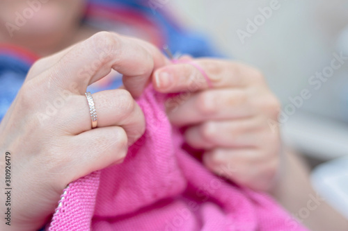 Woman knits with knitting needles pink sweater from natural woolen threads
