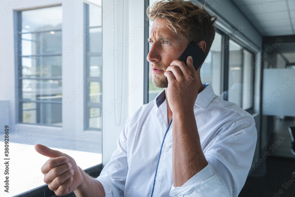 Young businessman talking on smartphone near the window at modern office Young businessman talking on smartphone near the window at modern office