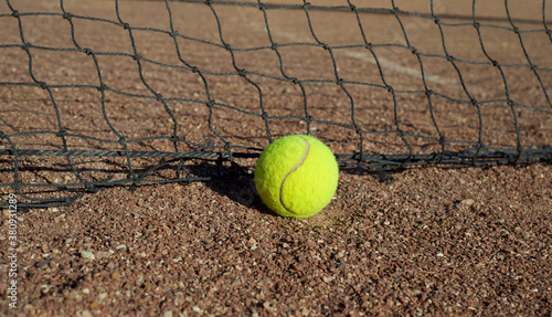  Tennis ball against the backdrop of a net on a dirt surface. © LKoroleva