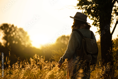 Silhouette of a woman wearing a hat and with a backpack at sunset. © scharfsinn86