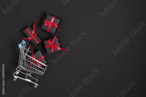 Shopping cart with presents top view on black background. Black Friday template for ad design of banners and flyers.