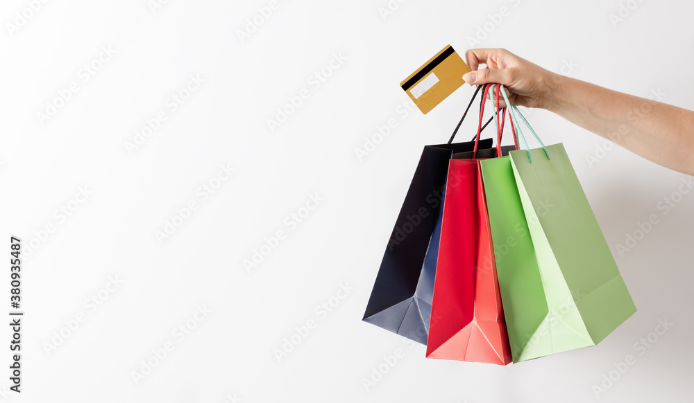 Woman hand holding group of colorful paper shopping bags and credit card over white background.