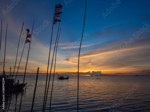 Silhouette of a fisherman boats during a beautiful orange sunset and dramatic blue sky background.