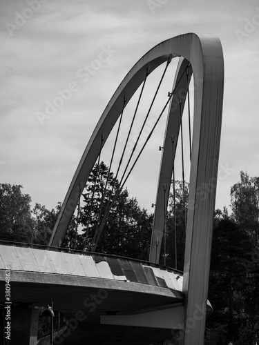 A close-up black and white shot of an arch walking bridge with reflecting glass railings. photo