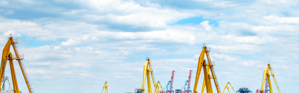 The tops of various cargo port cranes in the process of work against the background of the cloudy sky The tops of various cargo port cranes in the process of work against the background of the cloudy sky