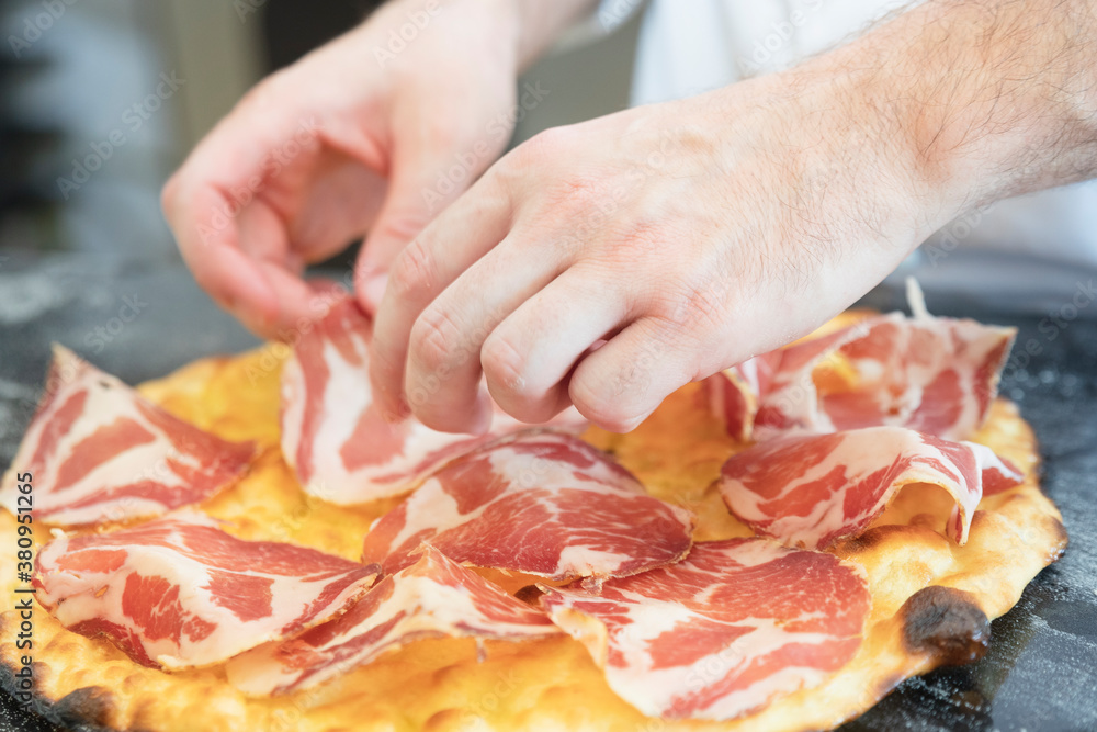 Italian cuisine: preparation of white pizza, with red ham, white mozzarella and green vegetables. Design serving. professional cook at work. food photography for menus and websites