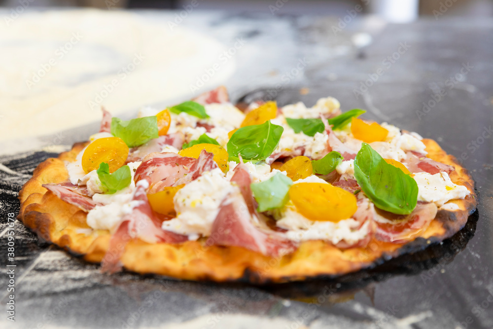 Italian cuisine: preparation of white pizza, with yellow tomatoes, white mozzarella, red ham and green basil. Design serving. professional cook at work. food photography for menus and websites Italian cuisine: preparation of white pizza, with yellow tomatoes, white mozzarella, red ham and green basil. Design serving. professional cook at work. food photography for menus and websites