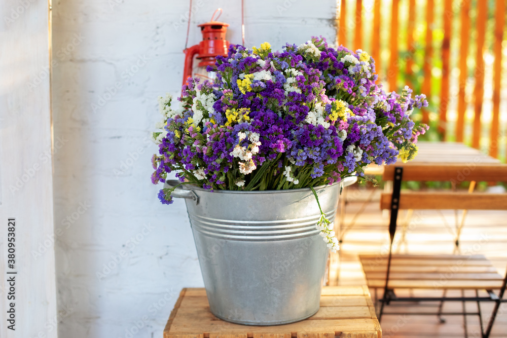 Bouquet of wildflowers in bucket on veranda home. Decor Autumn cozy terraces. Bunch Autumn flowers in vintage vase on table in garden. Home decor in rustic style. Cozy decor of patio yard. Flower shop