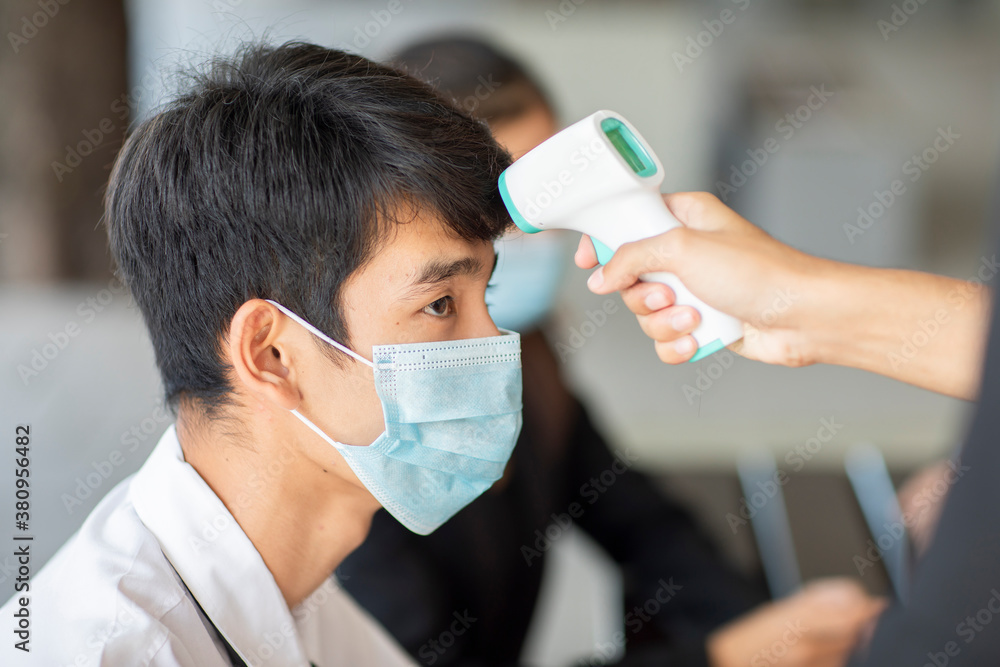 Young asian man getting his temperature taken with an infrared thermometer by a doctor during an outbreak
