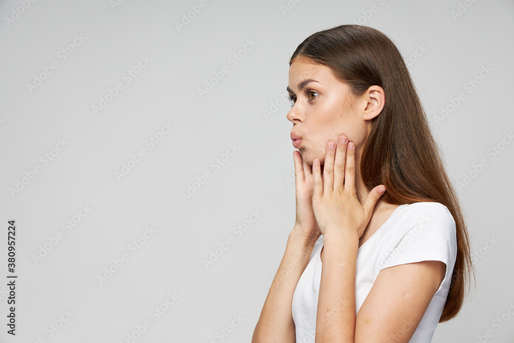 Woman holds hands on face look to the side white t-shirt light background Woman holds hands on face look to the side white t-shirt light background