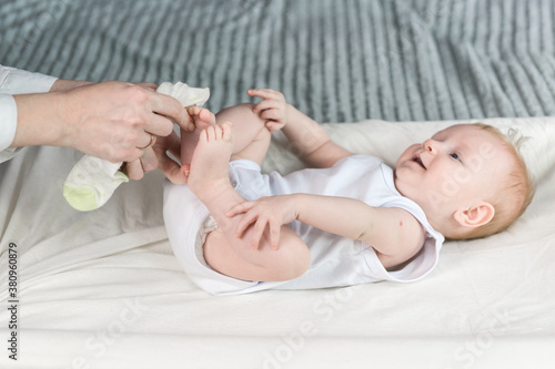 Mother puts socks on the baby. The baby is lying on the changing table and smiling © garmashevanatali