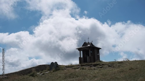 Small Old Wooden Chapel on Top of Mountain on Background Moving Clouds in Sky. photo