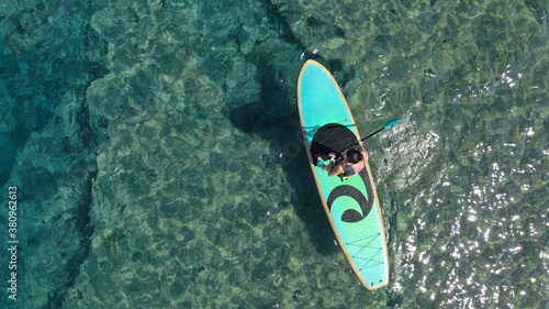 Aerial drone top down photo of unidentified woman exercising in SUP or Stand Up Paddle board in exotic island emerald beach