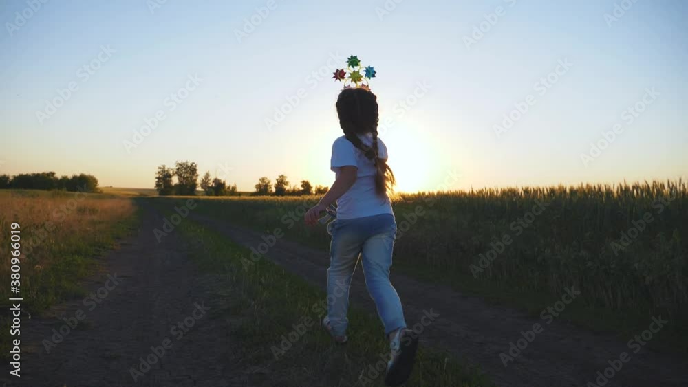 Happy child. A wind toy of different colors in the hands of a little girl. Sunset in a wheat field. A child runs with a toy at sunset. Freedom, the path to the dream.