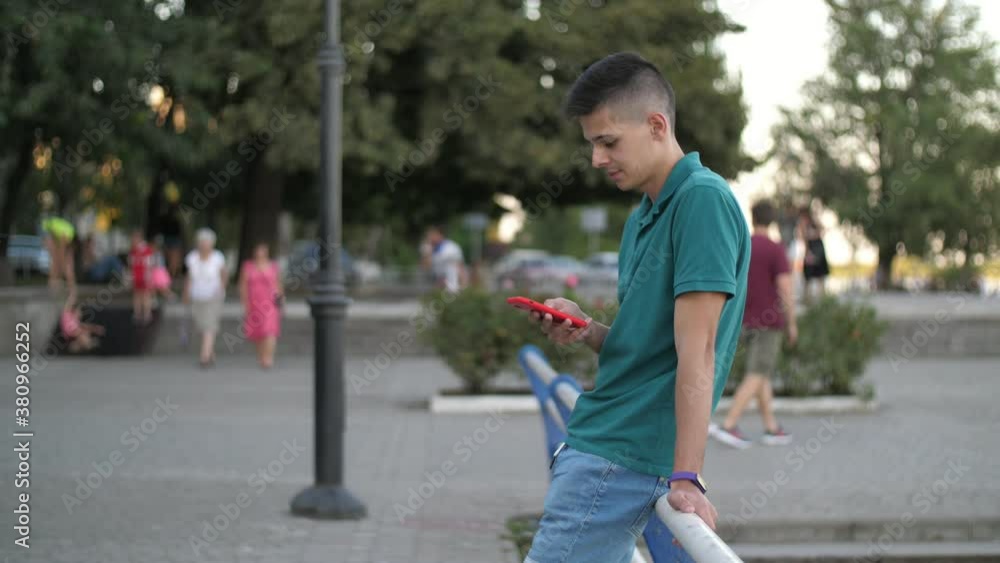 Smart guy standing on river embankment and surfing the net in summer in slo-mo Smart guy standing on river embankment and surfing the net in summer in slo-mo