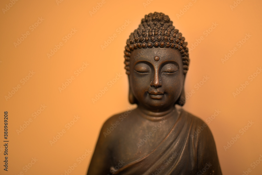 Peaceful bronze buddhist meditating Buddha head sculpture face sitting against simple bright orange wall with shadow
