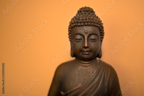 Peaceful bronze buddhist meditating Buddha head sculpture face sitting against simple bright orange wall with shadow