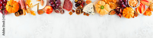 Fall charcuterie top border against a white marble banner background. Assorted cheese and meat appetizers. Copy space.